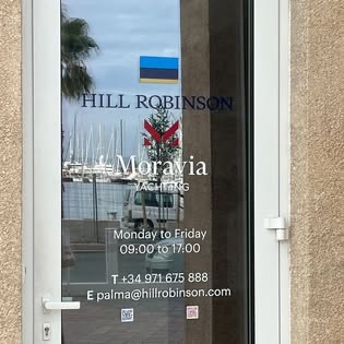 Printed window graphics with yacht-agency branding and opening hours on a glass door overlooking a Mallorca marina